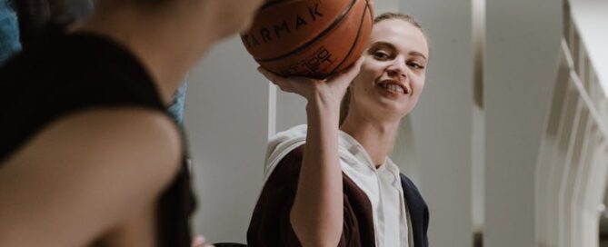 Two young women enjoying a playful moment with a basketball in a locker room setting.